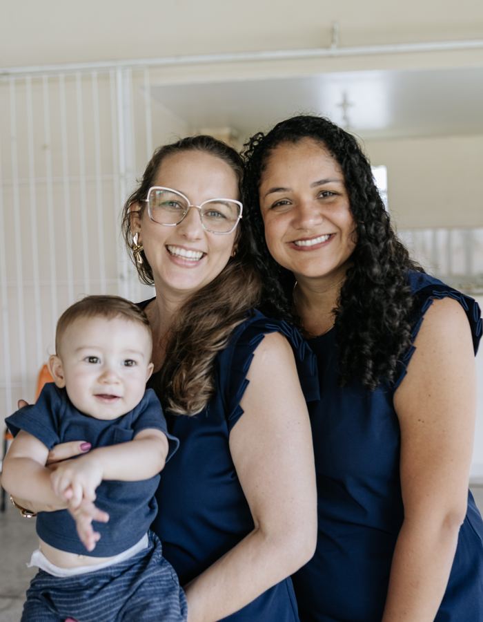 Manu e Stephanye abraçadas, sorrindo, com um bebê no colo