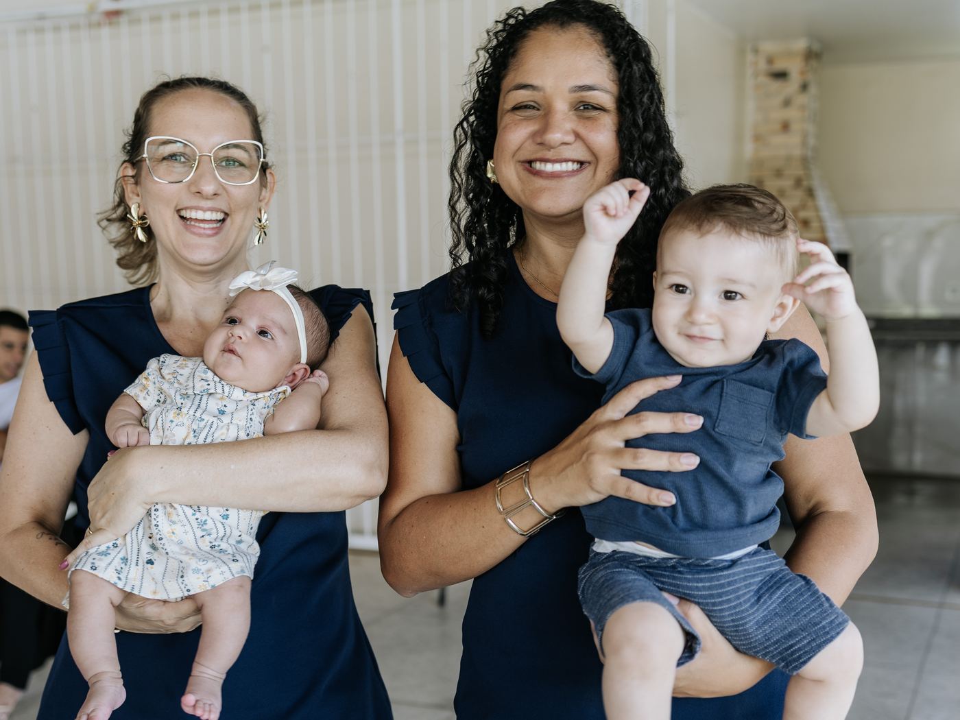Manu e Stephanye sorrindo, cada uma segurando um bebê no colo